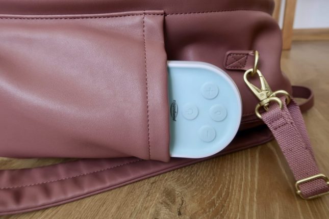 A pink rucksack style changing bag lying on it's side with a pumpables milk genie plus breast pump sticking out of the pocket https://oddhogg.com
