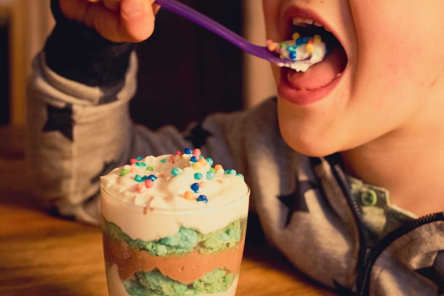 A child eating a layered dessert with sprinkles on the top
