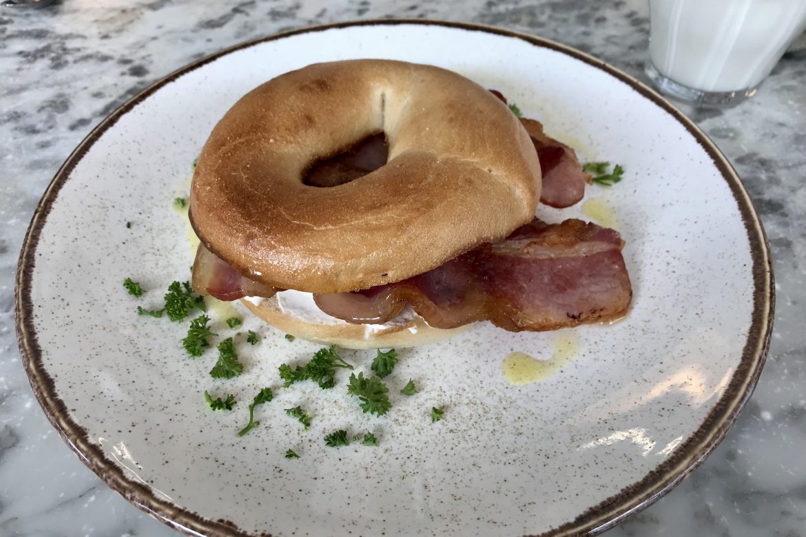 Bagel with cream cheese and bacon and a garnish on a plate in one of the places to eat in York with kids