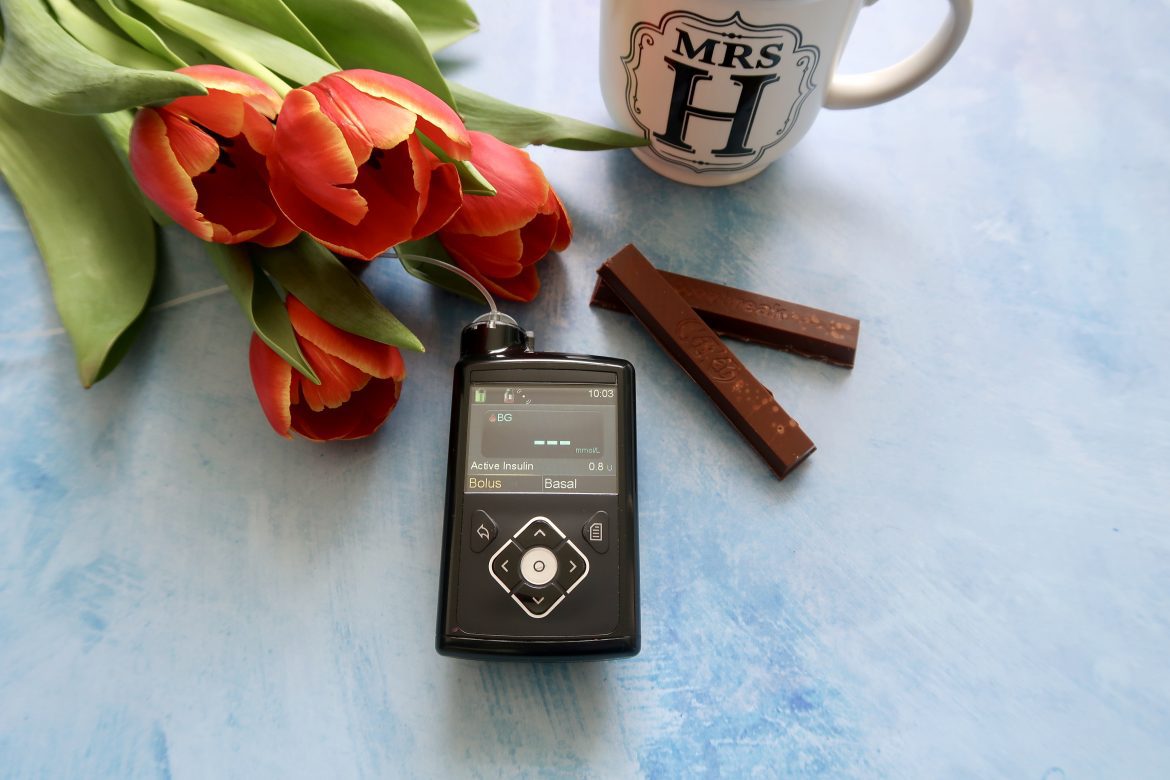 A pile of red tulips sits on a blue background with a mug with Mrs H written on it, a kit kat and an insulin pump