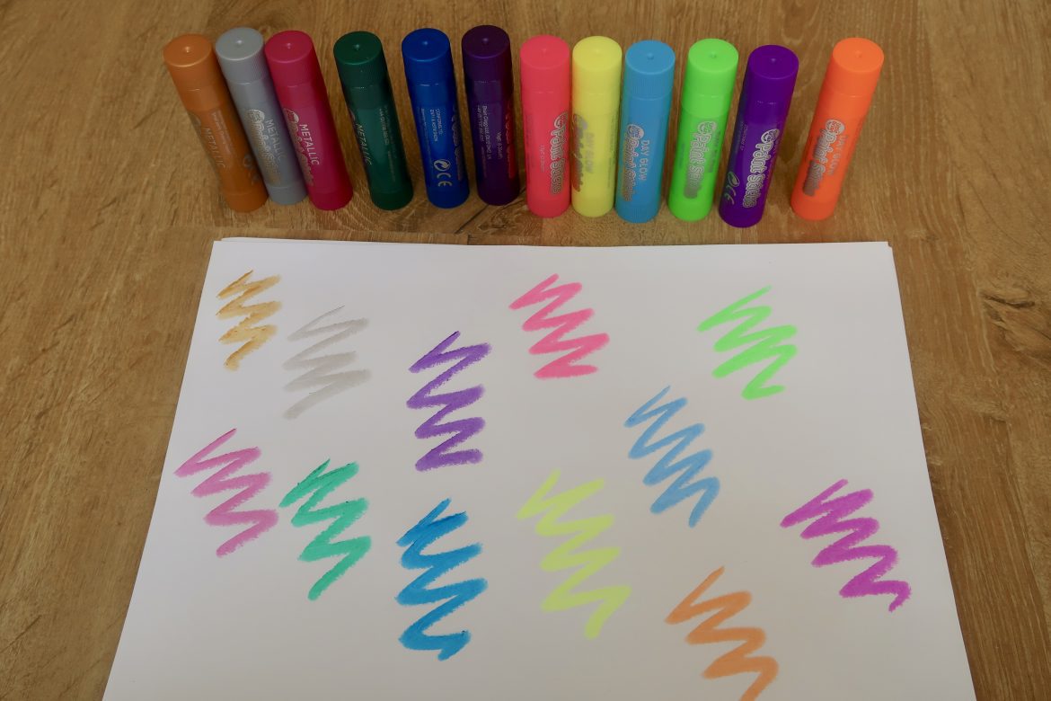 A range of Little Brian paint sticks behind a piece of paper with squiggles from each one drawn on it.