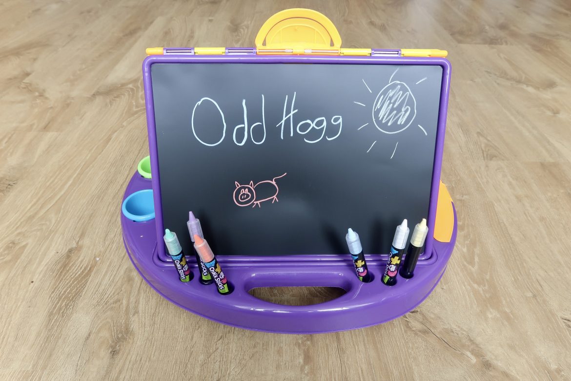 A small childs chalkboard with writing on it and a drawing of a pig in multicoloured paint