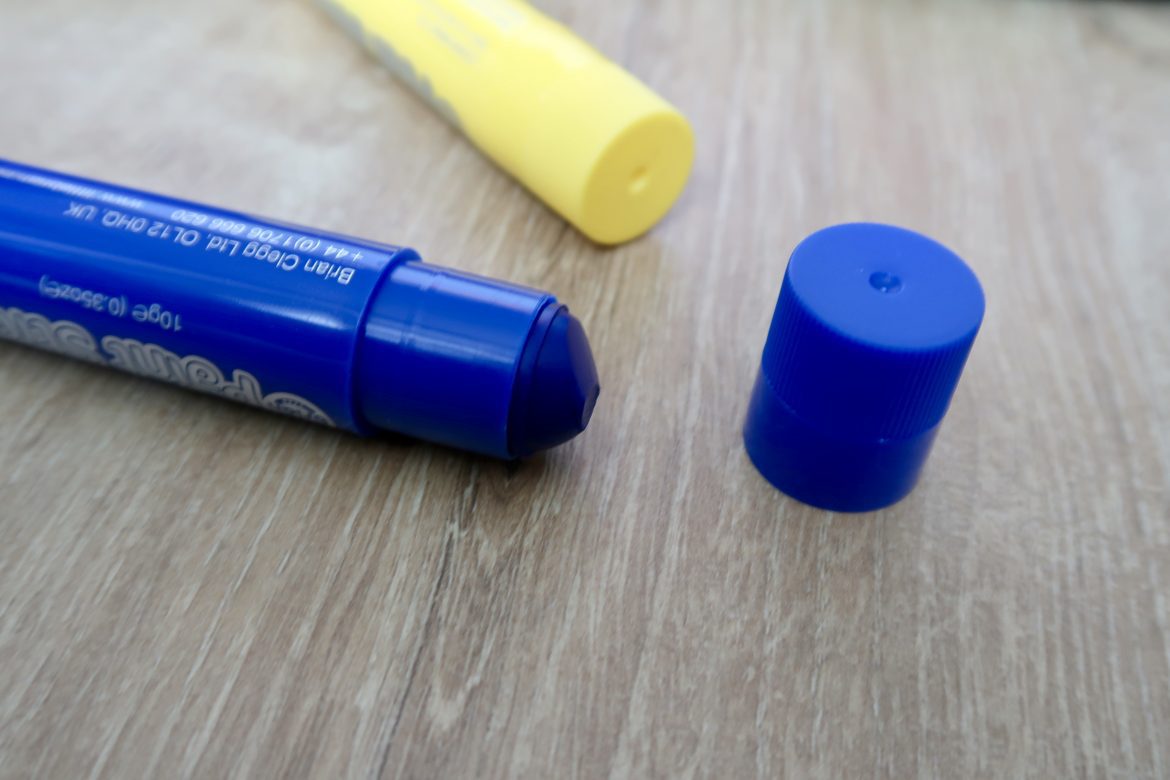 A blue paint stick and a yellow one lying on a wooden floor. The lid of the blue paint is off