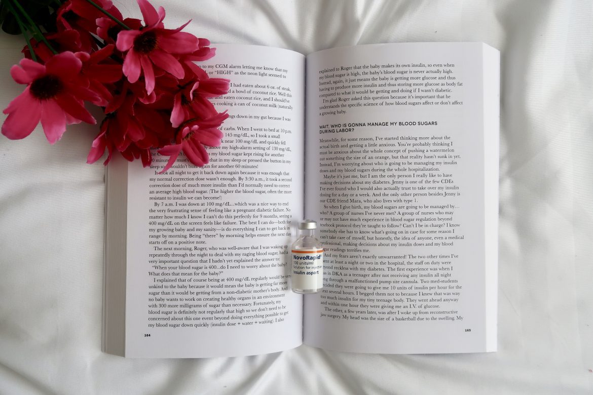 A type 1 diabetes book lying open with an insulin vial and a bunch of pink flowers covering the top left corner