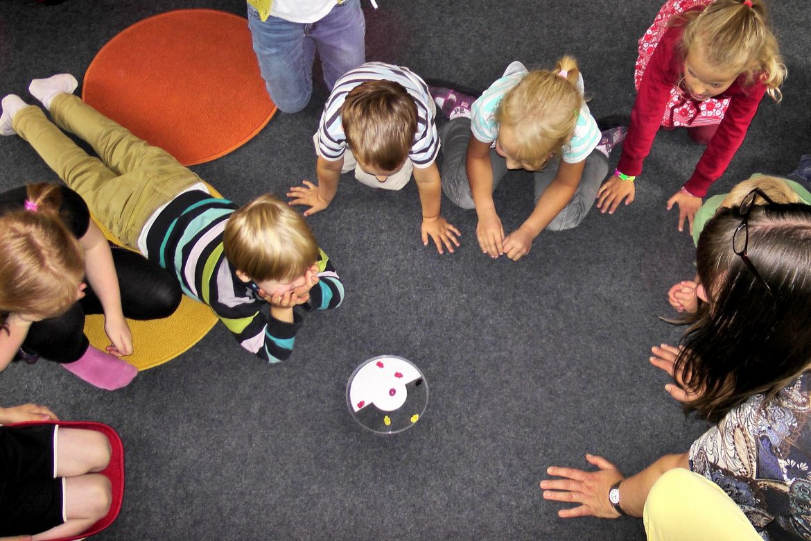 A group of children in childcare watching something on the floor with their teacher