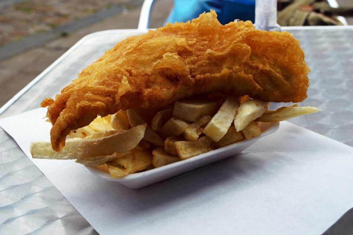 a takeaway dish of fish and chips on a metal outdoor table