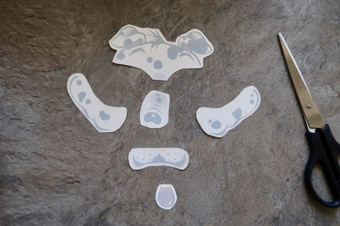 There are 6 face temporary tattoos that collectively look like a dogs face lying on a counter next to a pair of scissors