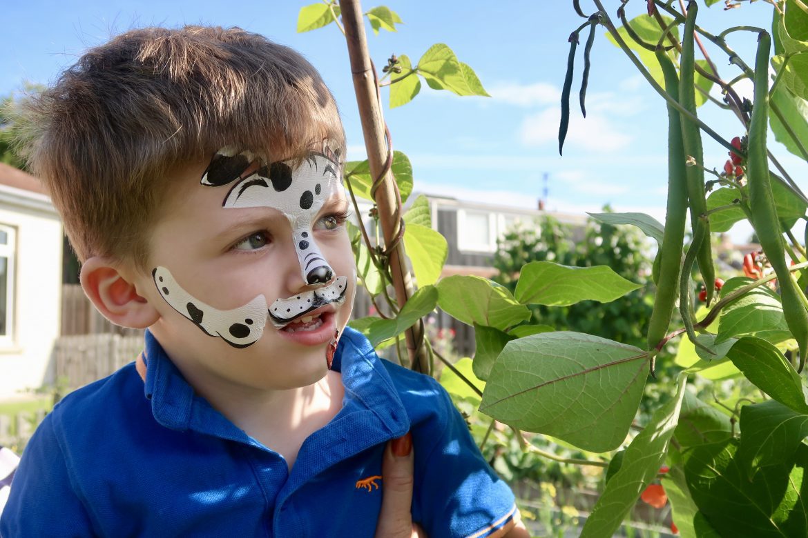 A boy looking at a plant with his face painted like a dog