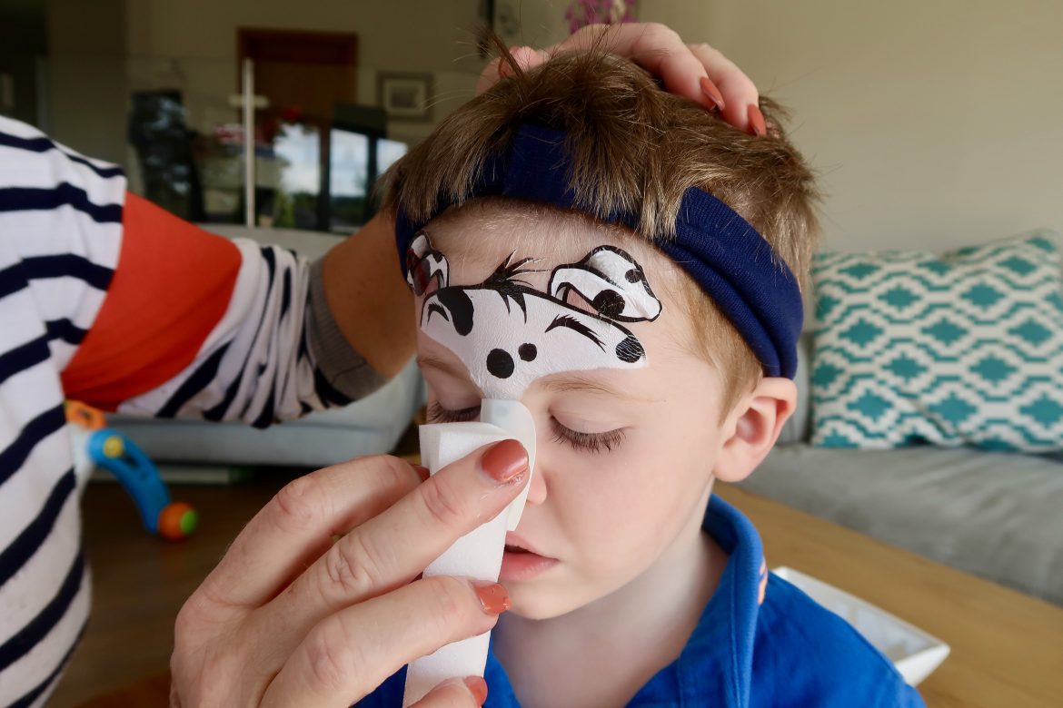 A boy having a temporary tattoo applied to his face with a sponge to make him look like a Dalmatian dog