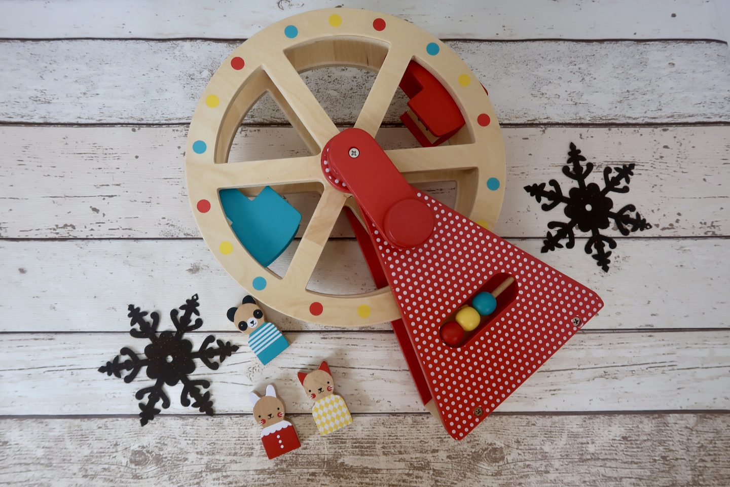 A wooden toy carousel lying on its side. It is surrounded by 2 brown metal snowflakes and 3 wooden toy animals