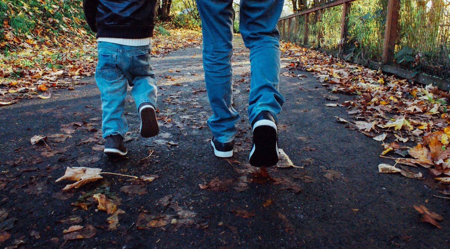 The legs and feet of a man and a child, walking away from the camera through the woods