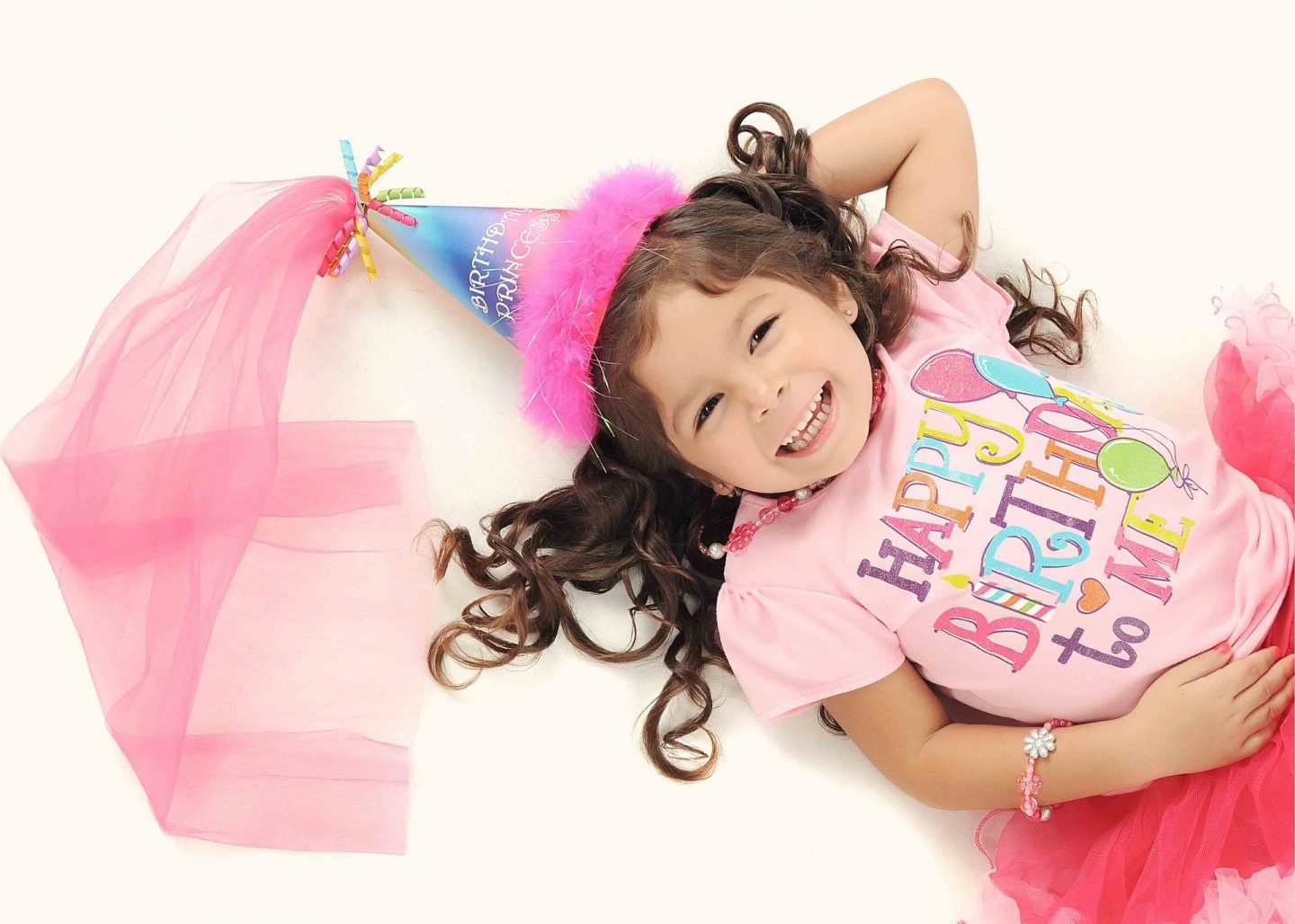 A little girl dressed in pink with a "Happy Birthday" t-shirt on and a crown