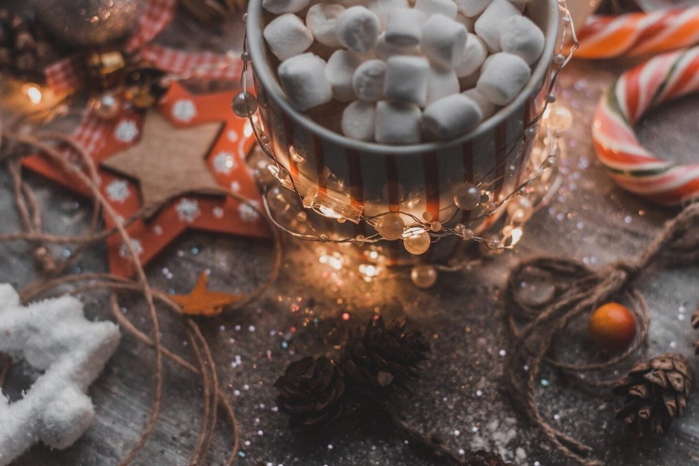 A table scattered with wooden stars, fairy lights, candy canes and a mug of hot chocolate with marshmallows