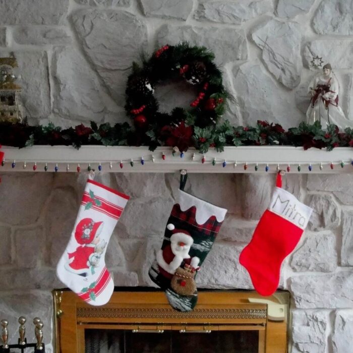 3 stockings hanging on a mantle piece, with a Christmas wreath above