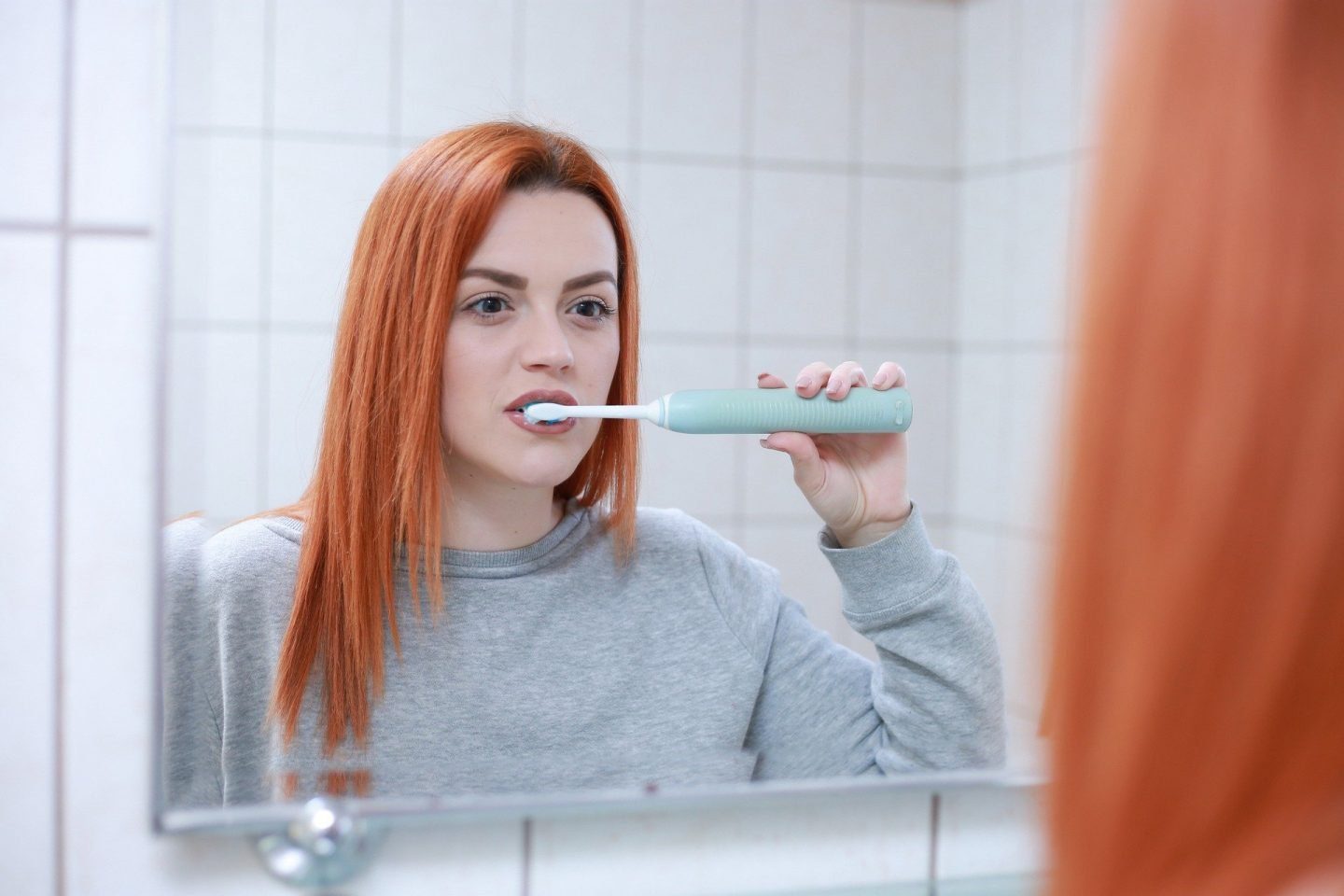 A woman looking in a mirror brushing her teeth with an electric toothbrush