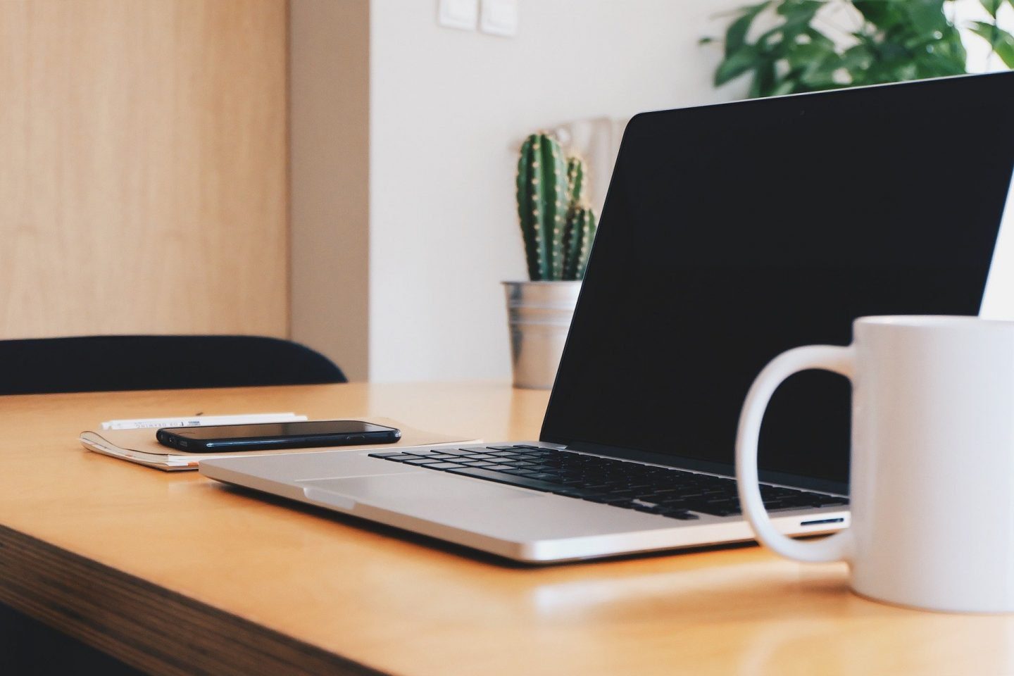 A laptop on a desk next to a mug and a mobile phone