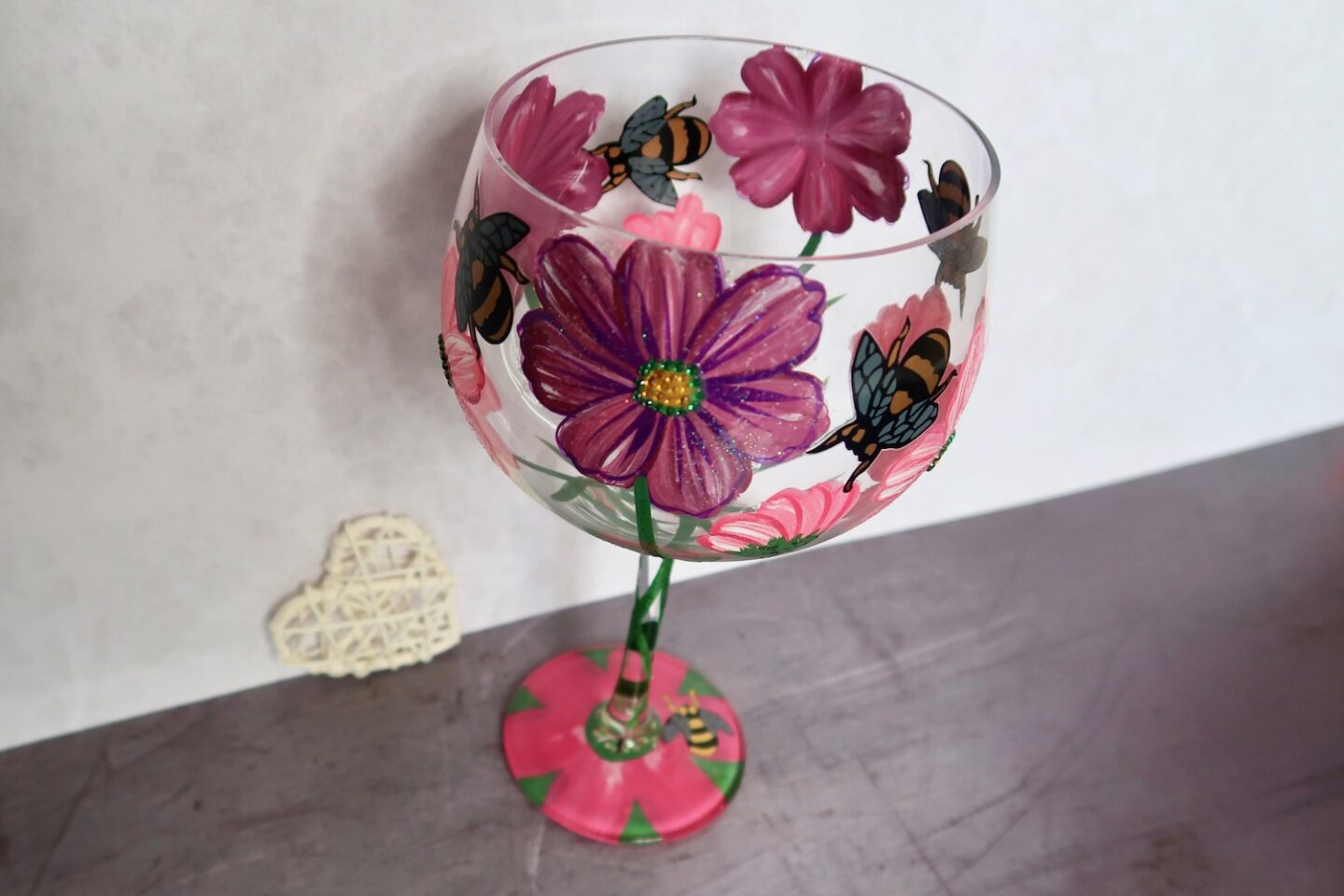A gin glass painted with pink flowers and bees