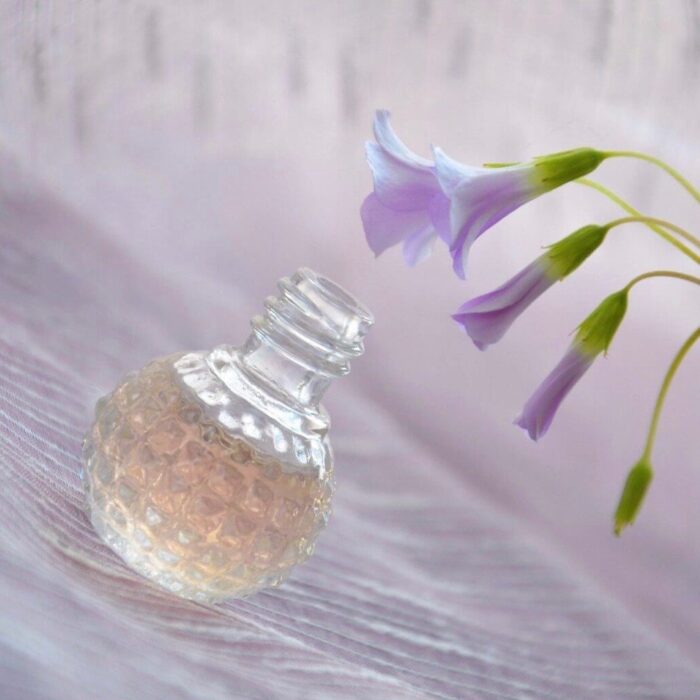 A bottle of perfume next to some purple flowers.