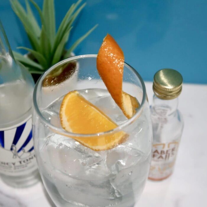 A glass of gin with a slice of orange in it, next to a miniature gin bottle.