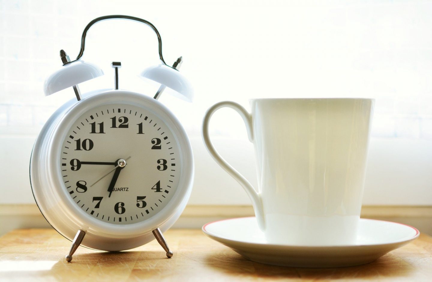 A white alarm clock showing the time as 6:45, sitting next to a cup and saucer
