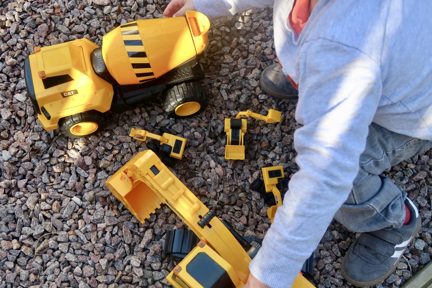 A top down view of a child playing with yellow construction vehicle toys