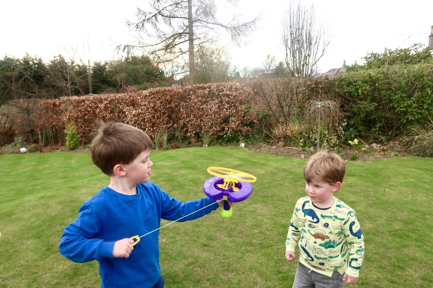 2 children in the garden. One is holding a helicopter bubble toy and pulling the string