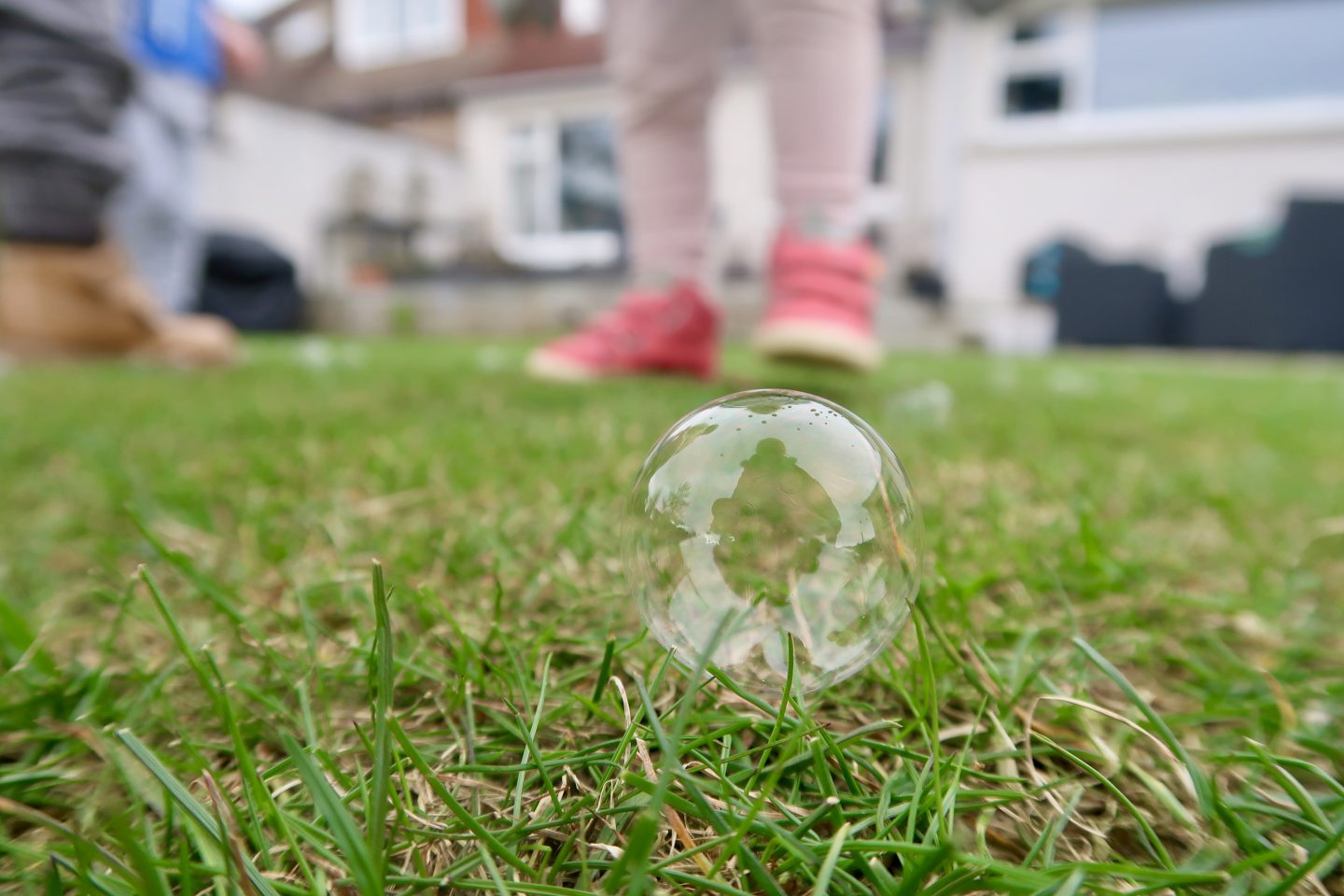A bubble sitting on grass with childrens legs behind it