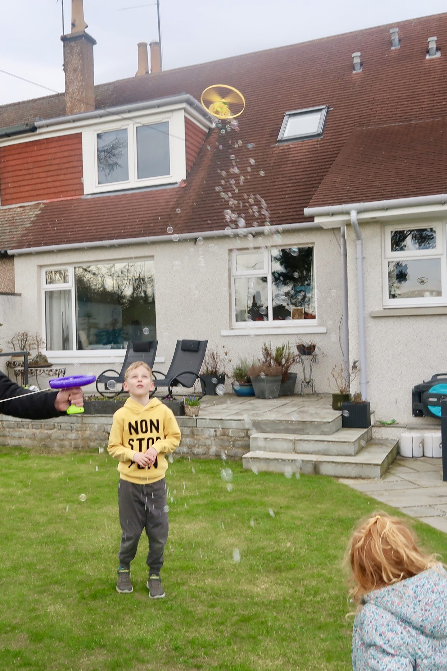 Children standing in a back garden watching a helicopter bubble toy in the sky