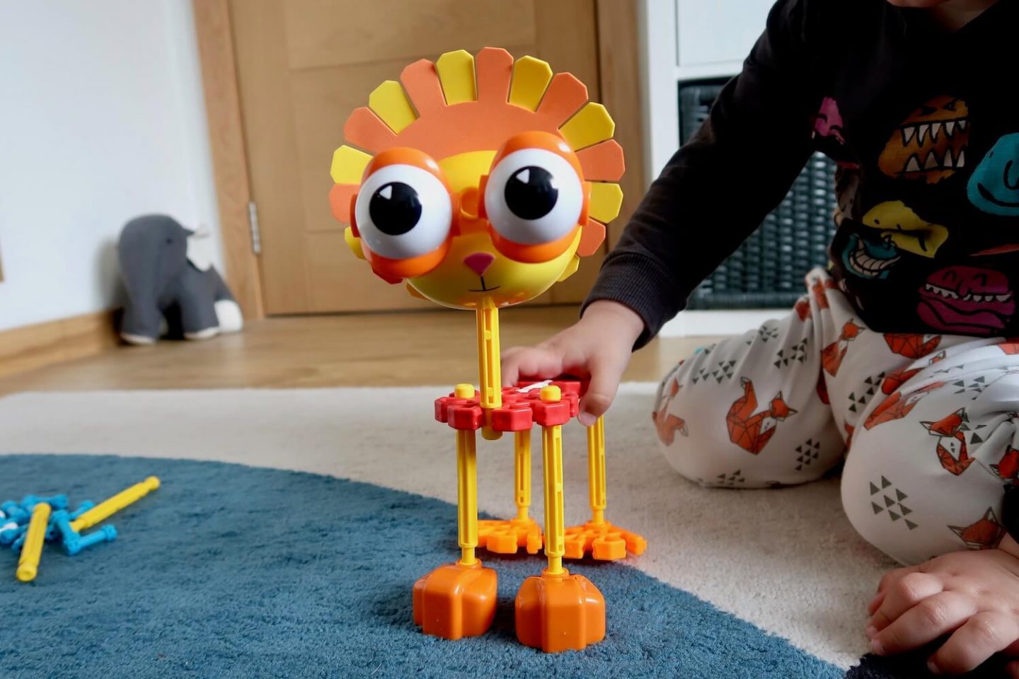 A lion made out of K'Nex with a child's hand on it's back