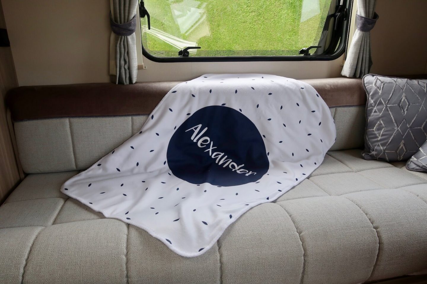 A white blanket with blue flecks and a large blue circle in the centre, on the seat of a caravan