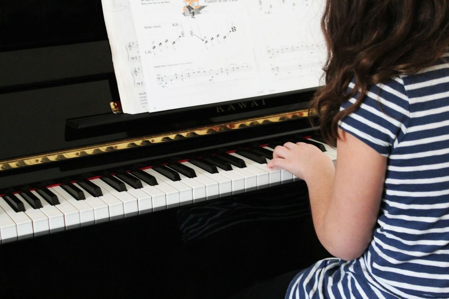 A black piano with a girl in a blue and white striped dress on