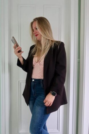 A woman in a black blazer and a pink lace bodysuit with jeans