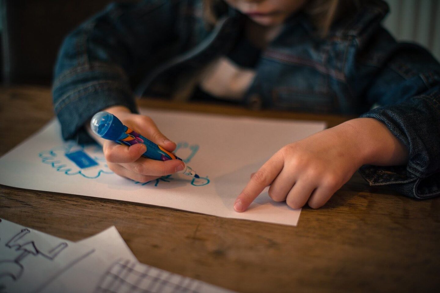 A child drawing on a piece of paper with a blue pen