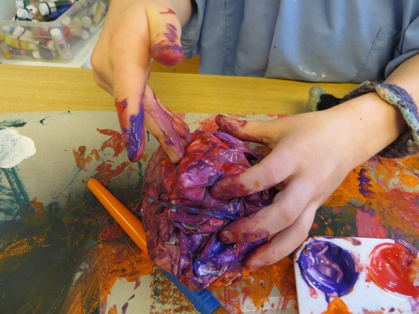 Hands holding a painted model, with paint splatters and brushes on the table below
