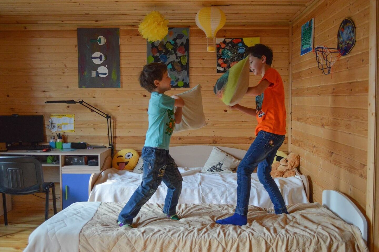 Two boys standing on a bed having a pillow fight