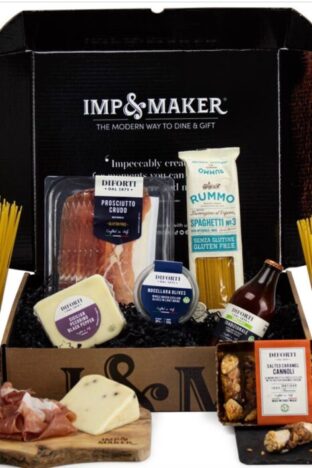 A cardboard box open with Italian food displayed in it. There is hams, pasta and cheese