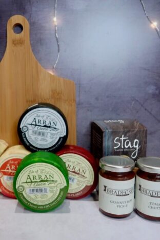 A wooden board, with cheese rounds in front and 2 jars of chutney next to it