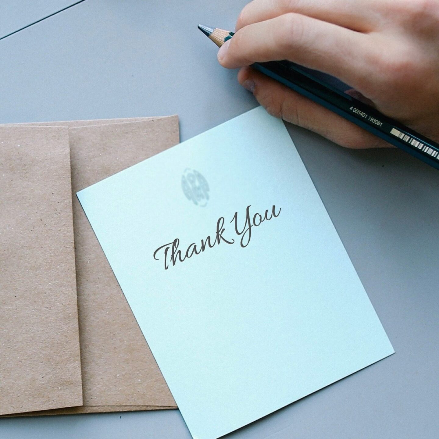 A hand holding a pen, next to a piece of note paper with "Thank you" written on it