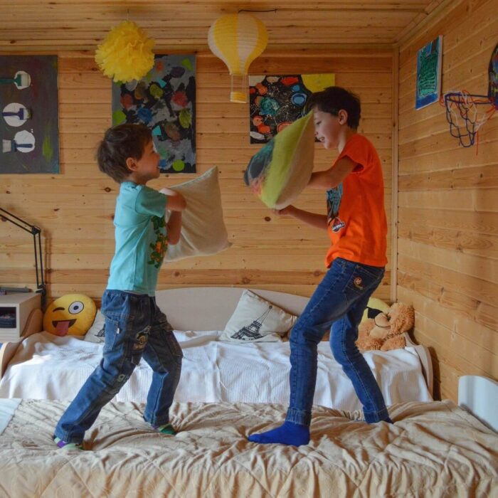 Two boys standing on a bed having a pillow fight