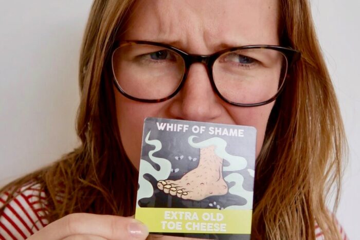 Woman smelling a card with "whiff of shame" written on it and a picture of a foot
