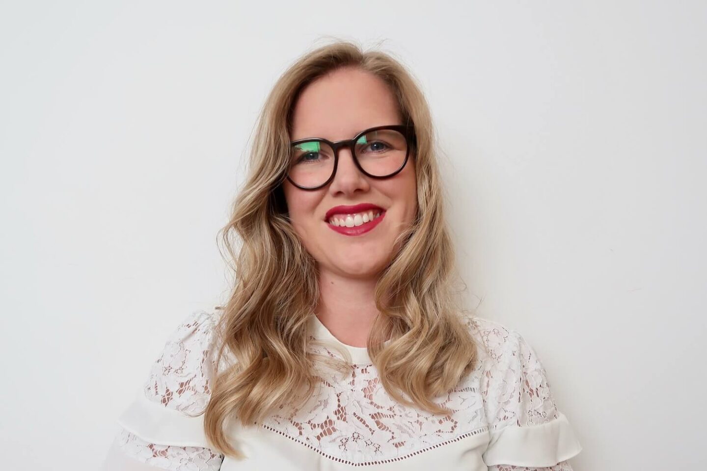 A girl with blonde wavy hair, red lipstick and glasses smiling