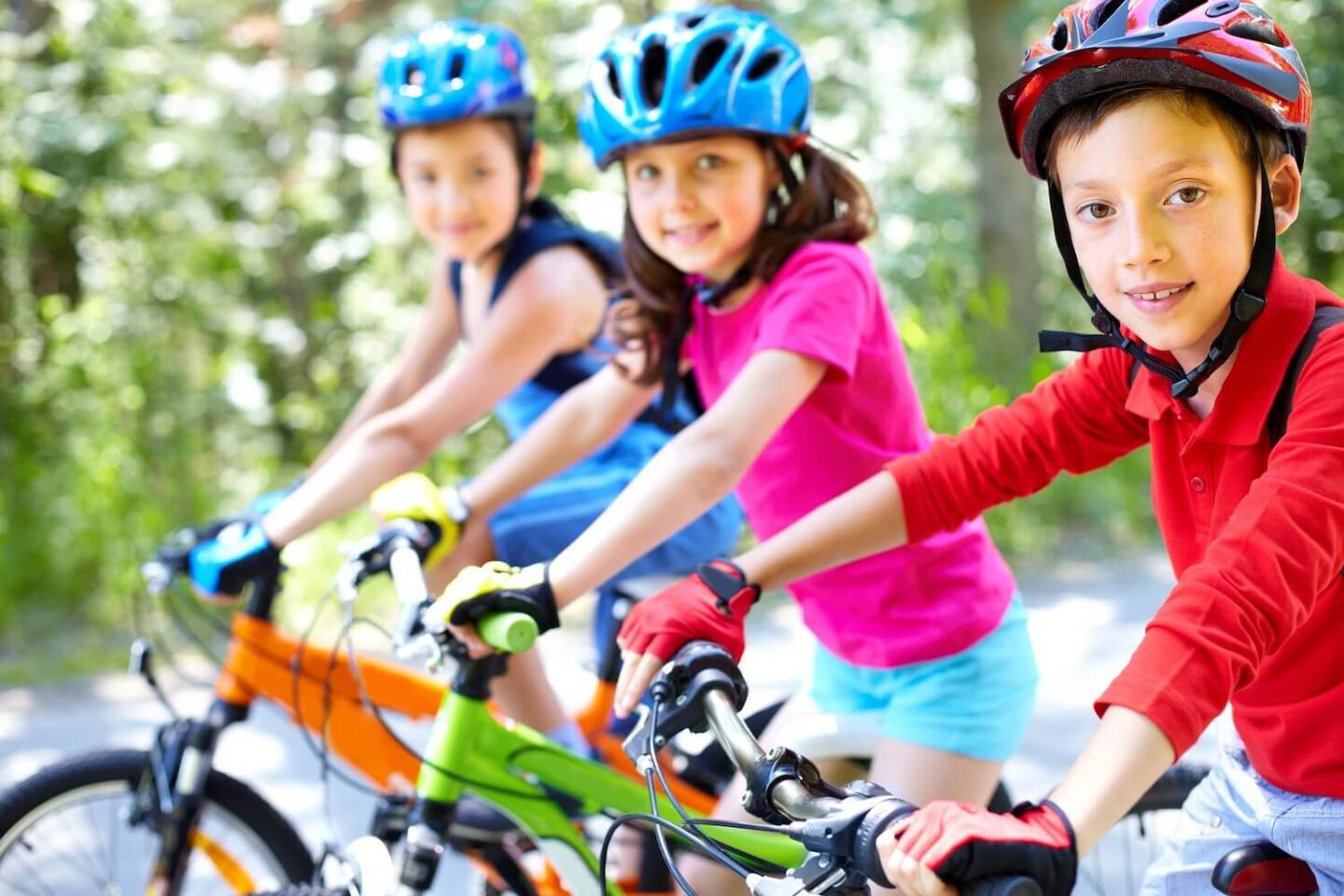 Three children on bicycles and helmets looking at the camera