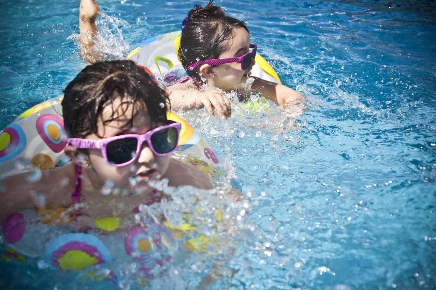 2 young girls in a swimming pool wearing sunglasses and rubber rings