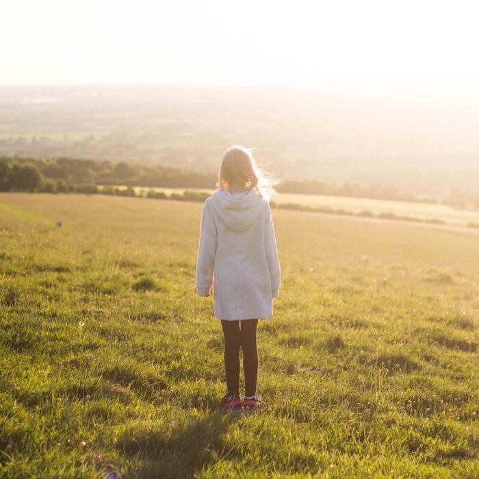 A girl standing on a grassy hill looking out over the countryside