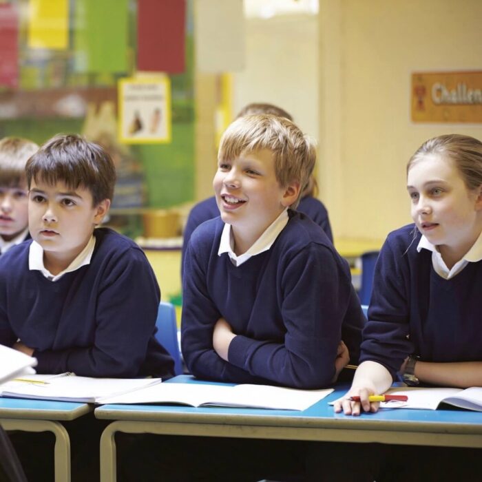 3 children in a blue school uniform sitting at a school desk