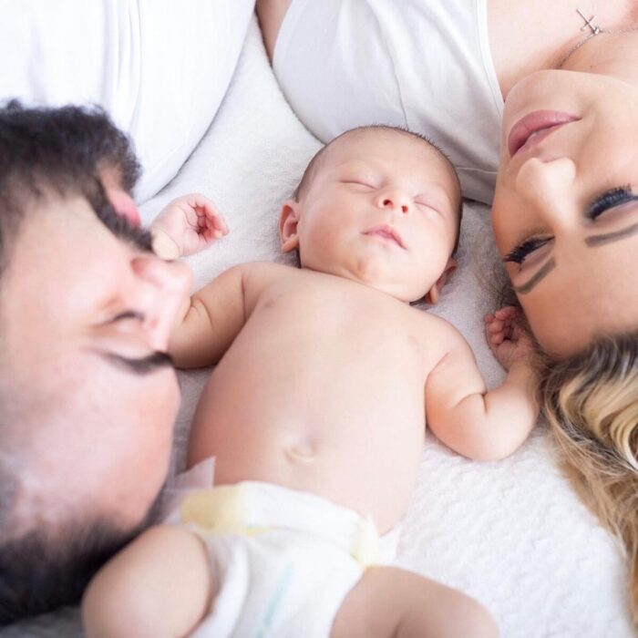 Mother and father lying on either side of a newborn baby asleep.