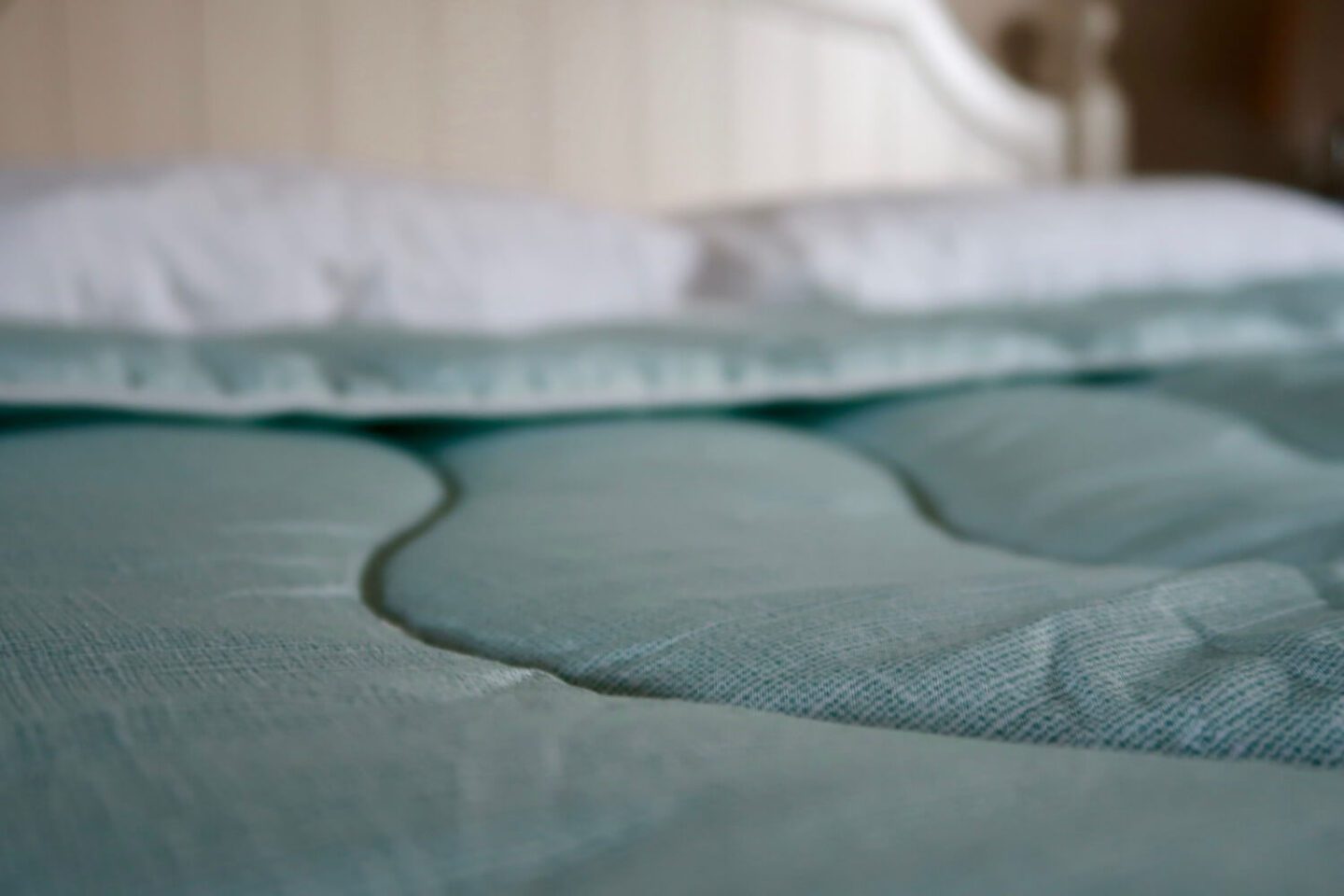 A green coverless duvet on a cream bed with white pillows