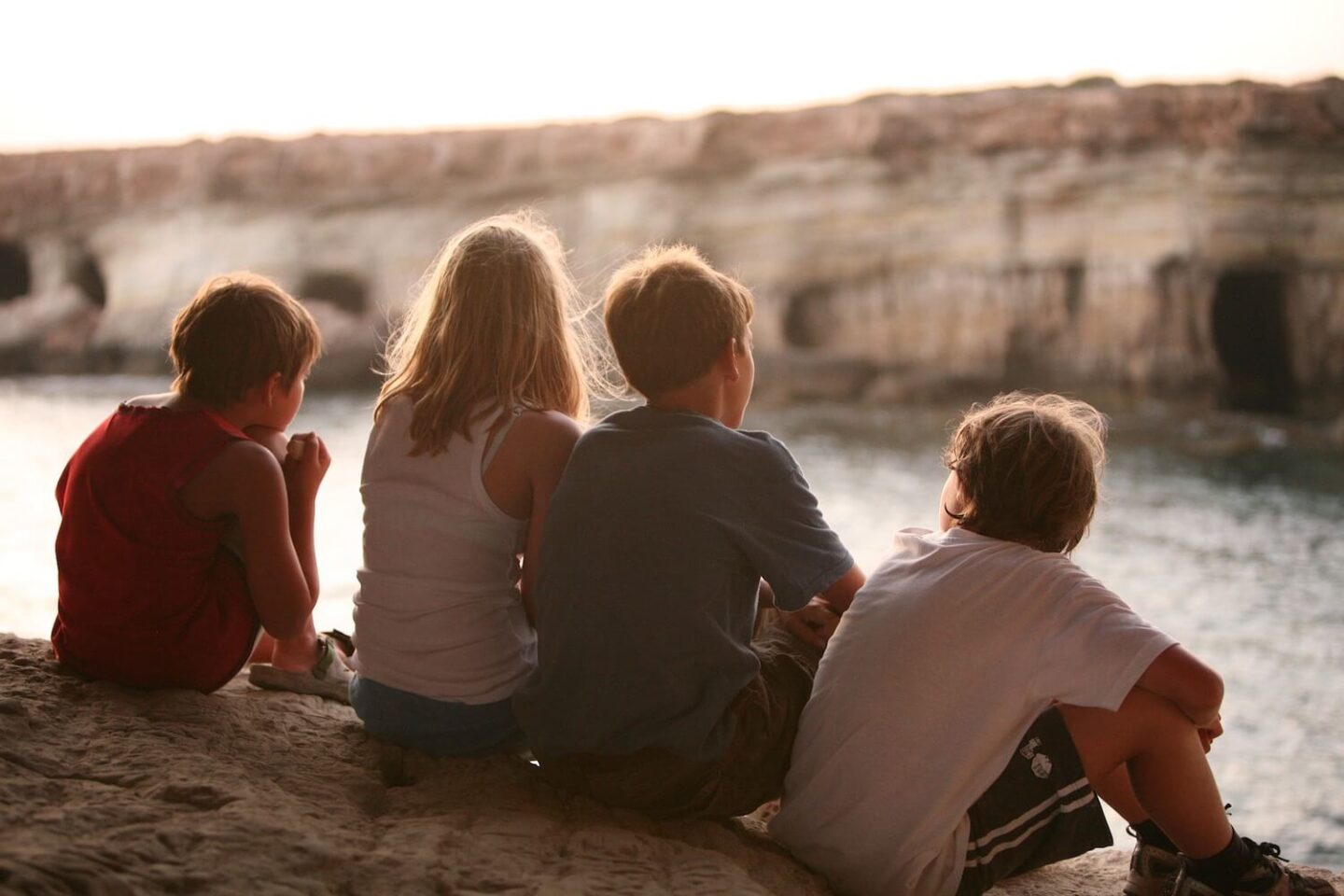 4 children sitting on a ledge and looking out over some water