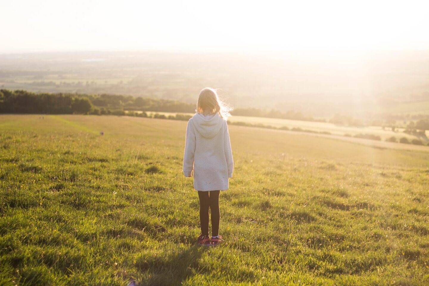 A girl standing on a grassy hill looking out over the countryside