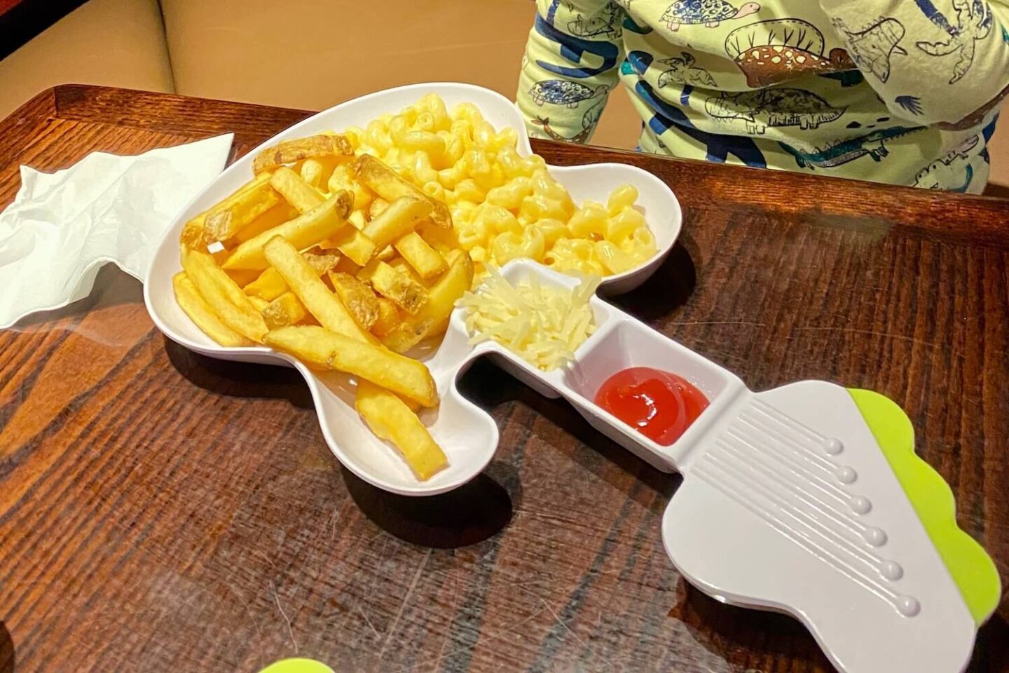 A child's plate shaped like a guitar with macaroni cheese and chips on it